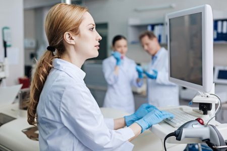 New technologies. Pretty lab assistant sitting in profile looking forward while working with pleasure