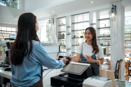 Friendly Asian Café Owner Accepting Contactless Payment From Customer - Modern Payment Solutions. Female customer using credit card