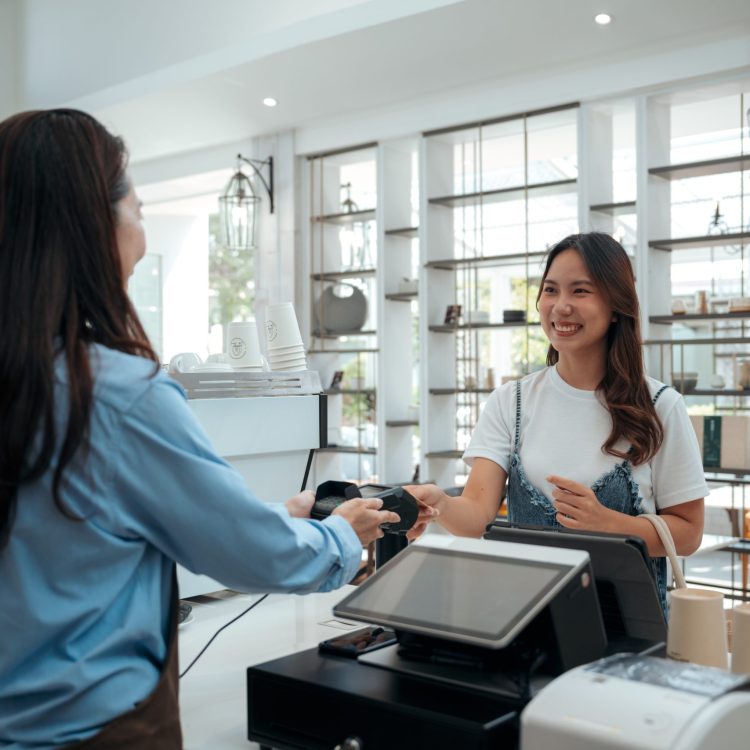 Friendly Asian Café Owner Accepting Contactless Payment From Customer - Modern Payment Solutions. Female customer using credit card